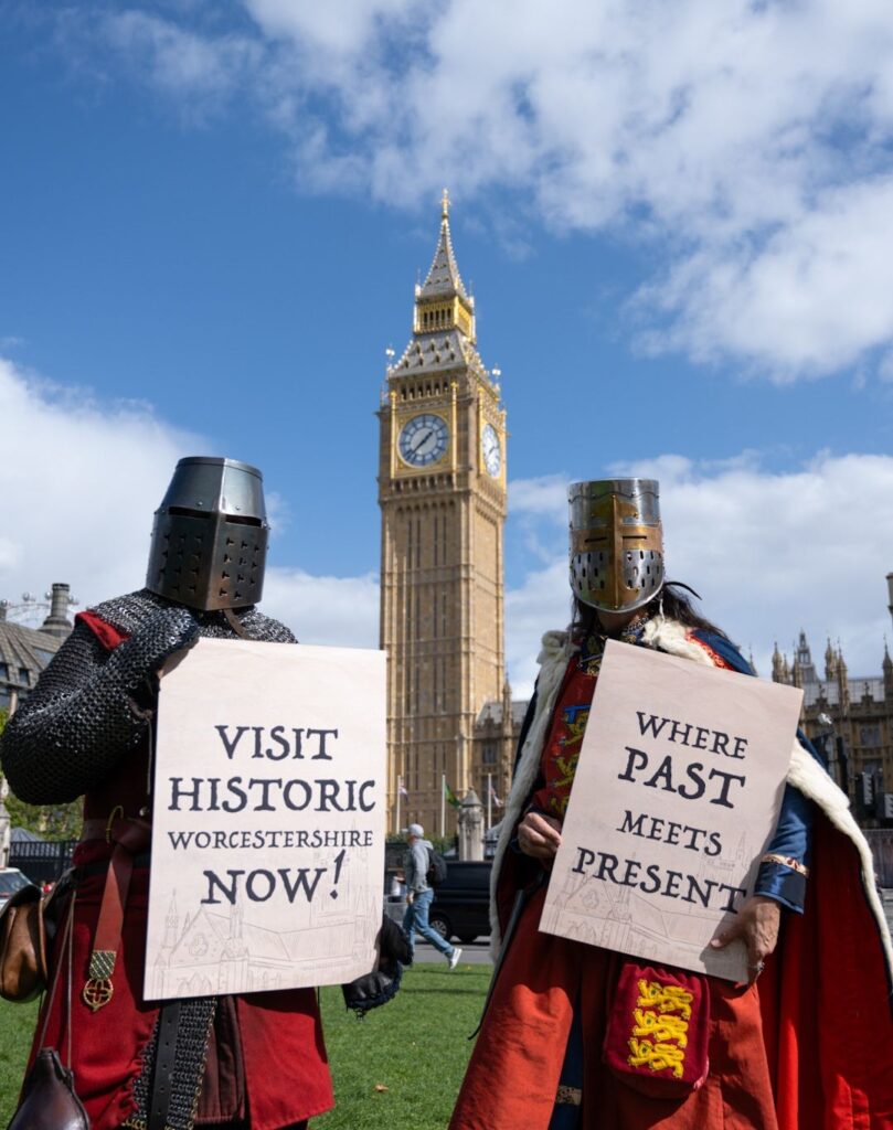 2 knights holding signs saying Visit Historic Worcestershire Now! Where Past Meets Presents. In front of Big Ben in London.