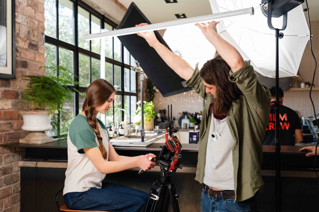 Side view of girl with plait wearing white and green t-shirt on her phone in front of camera. DOP holding tube light above her head. Shot for Luceco TV ad.