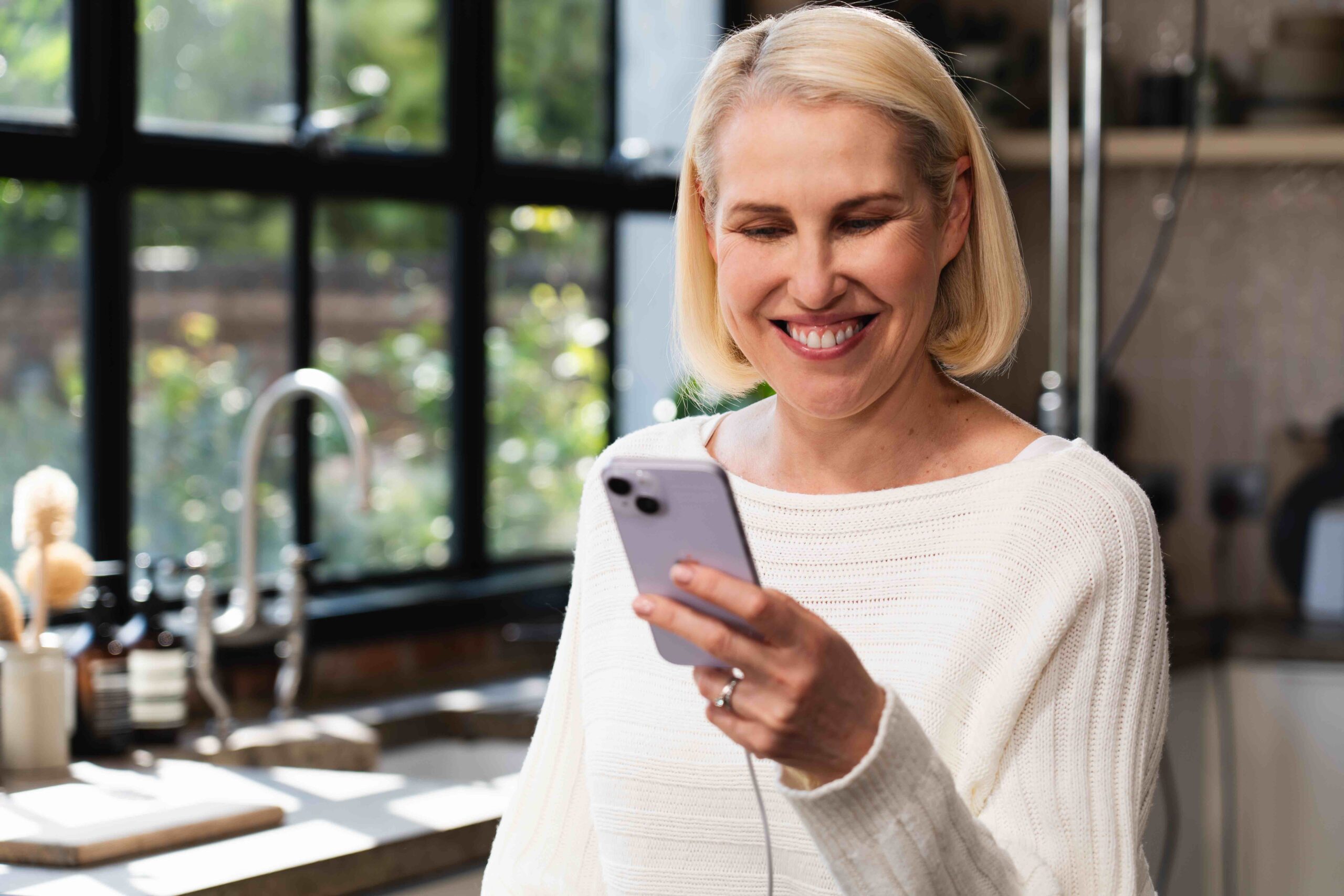 Blonde woman wearing white jumper looking at phone plugged into charger for Luceco TV ad