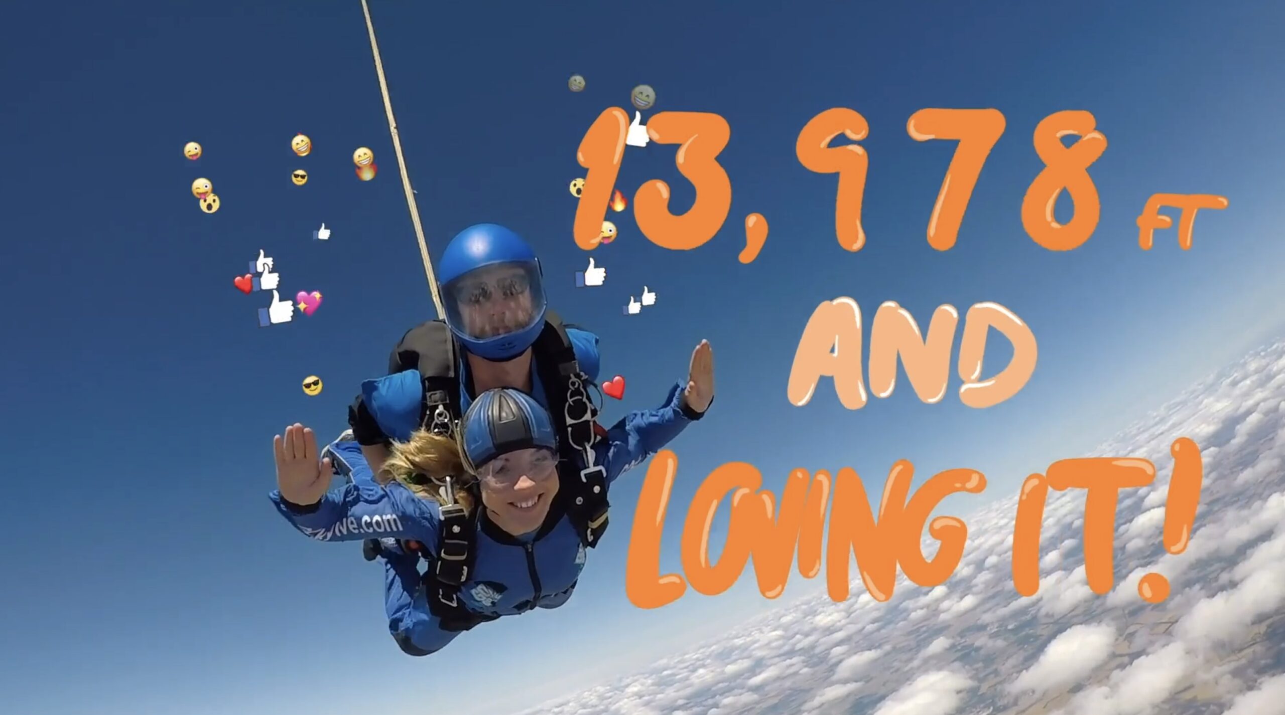 A man and a woman sky diving in the sky looking at camera. Animated orange text reads 13,978ft and loving it! Emojis, likes, and hearts surround them.