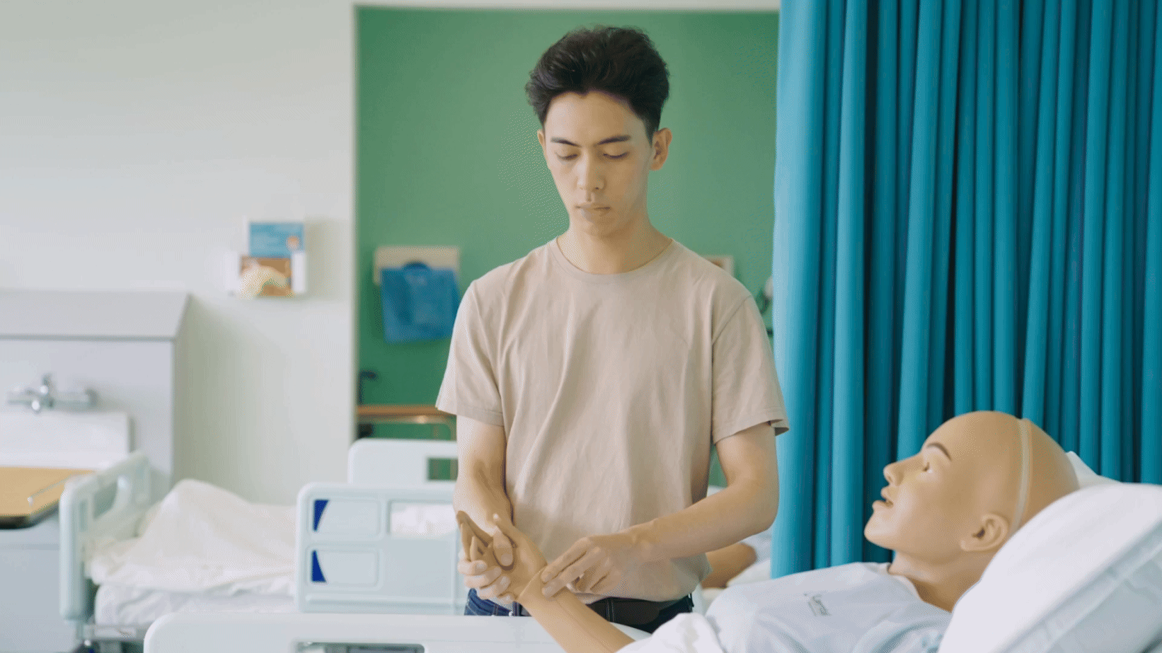 A male medical student checking the pulse of a manikin in a hospital bed. He is stood up staring directly at camera. South and City College Birmingham logo moves over the screen revealing the same student in a different environment - a hospital, checking the pulse of a real patient. He is now wearing medical scrubs. This is his dream career.