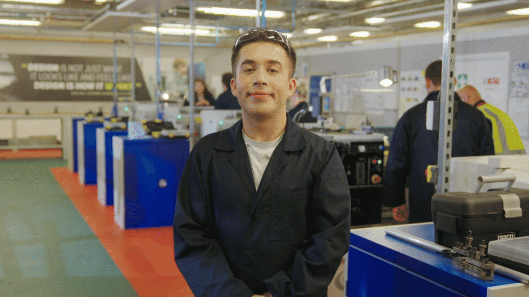 A man in coveralls in an engineering classroom stood up staring directly at camera. South and City College Birmingham logo moves over the screen revealing the same student in a different environment - a real engineering lab. His dream career. Pink and white text reads: The Real World.