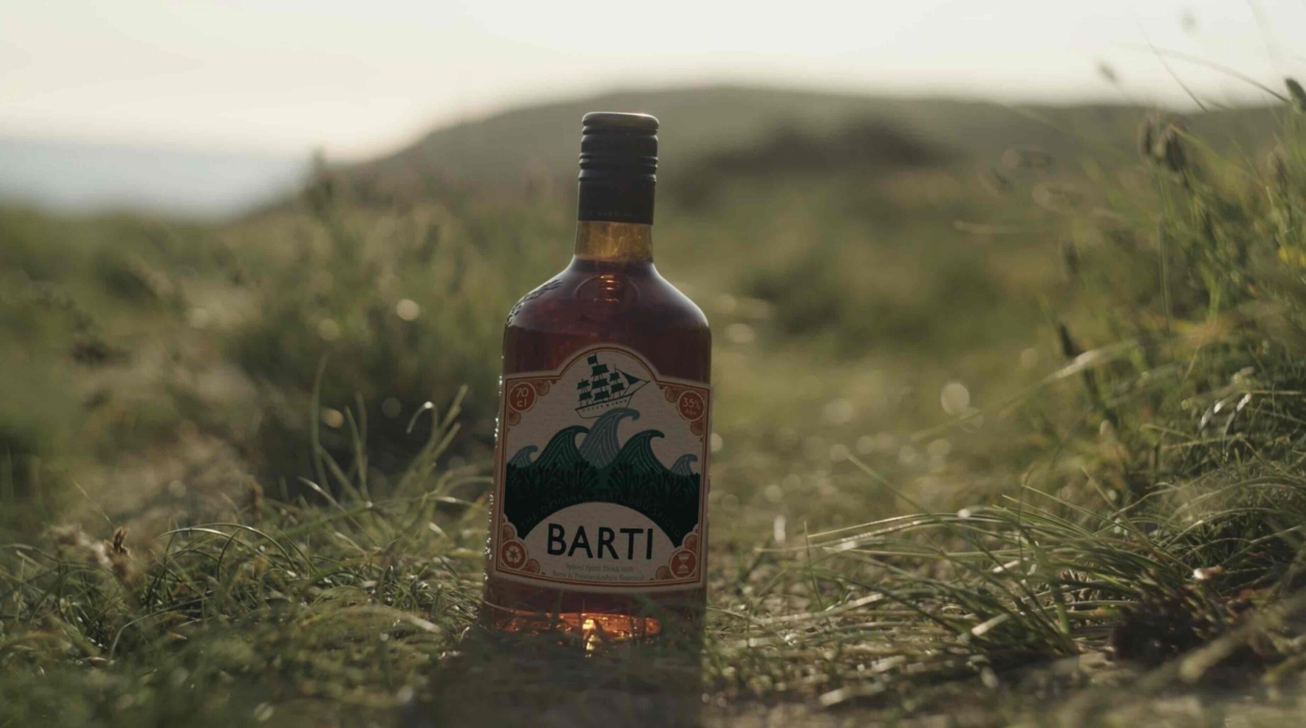Barti Rum bottle in a field. Illustrated logo with ship riding some waves.