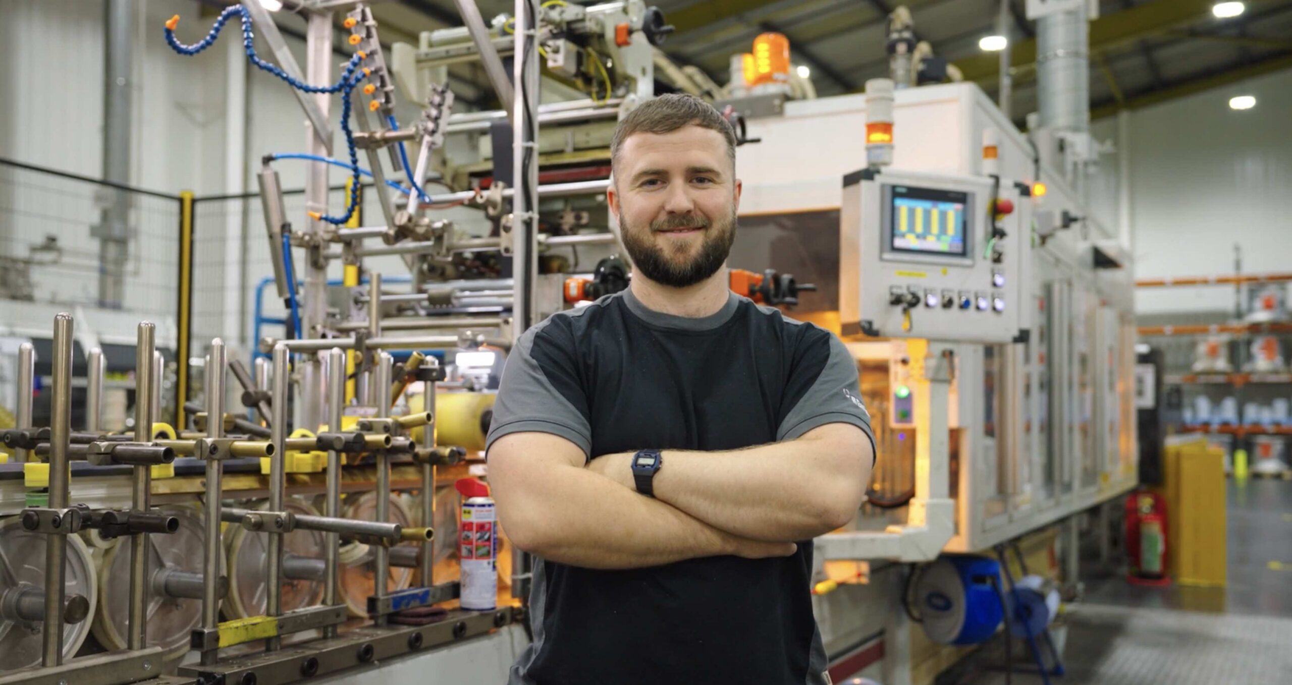 Male factory worker inside manufacturing plant with arms crossed staring directly at camera