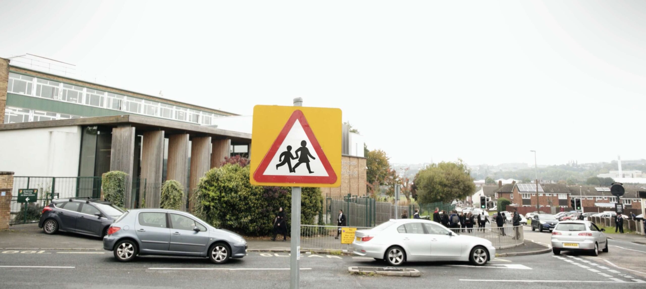 Street sign on busy street showing warning triangle with silhouette of parent and child walking.
